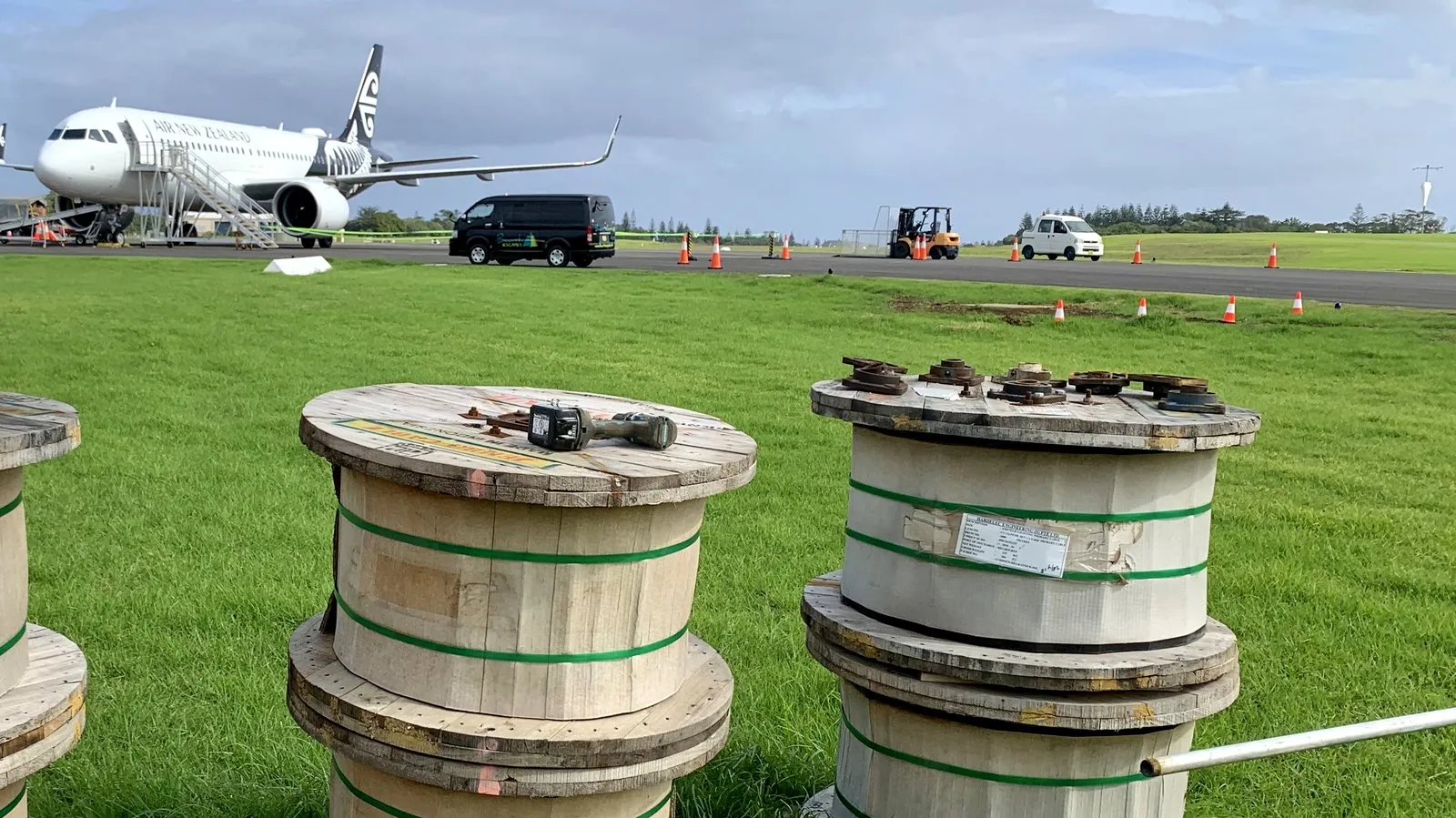 Primary cable drums beside the airside works at Norfolk Island Airport with an aircraft on the runway behind