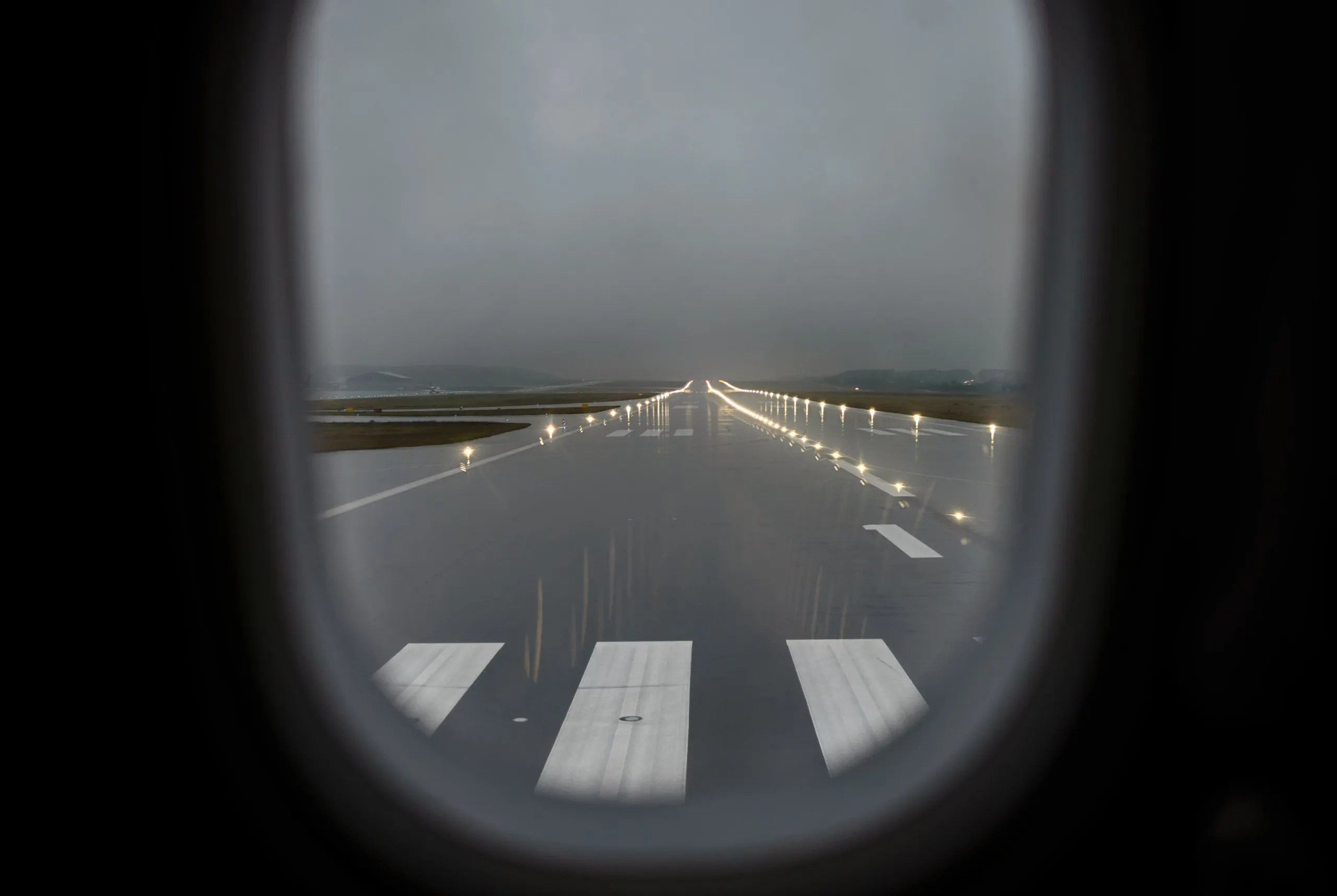 Wet runway with edge lighting seen through an aircraft window